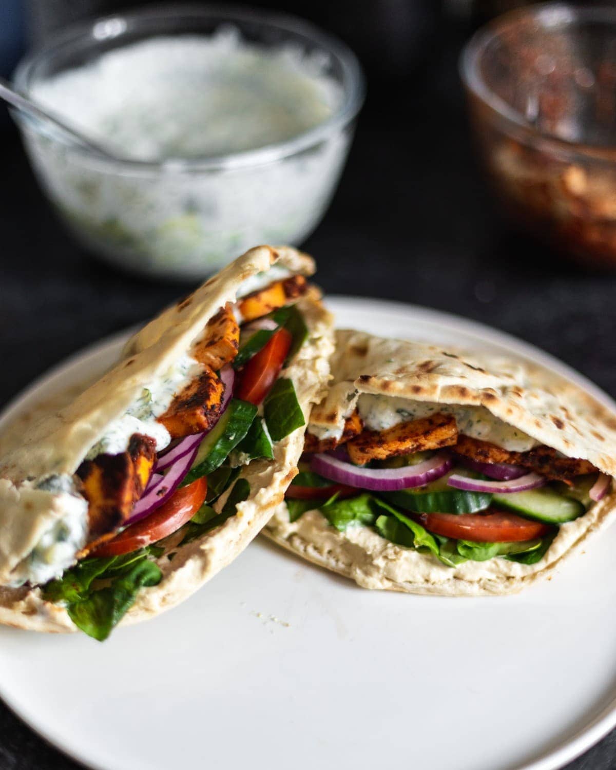 A plate with two pittas, loaded with salad, marinated tofu and tzatziki.