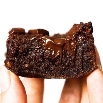 Someone holding up a slice of vegan chocolate brownie in front of the camera, with melted chocolate oozing from the middle.
