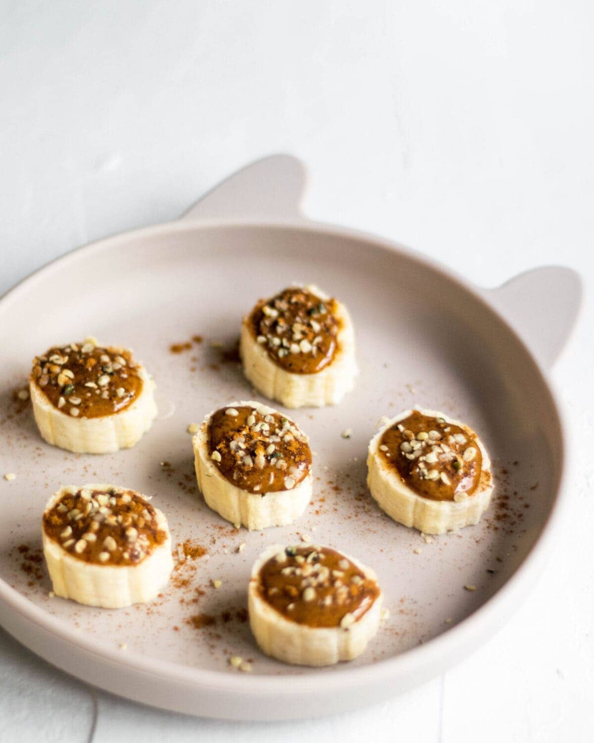 Childs plate with slices of banana, topped with almond butter, hemp seeds and cinnamon.