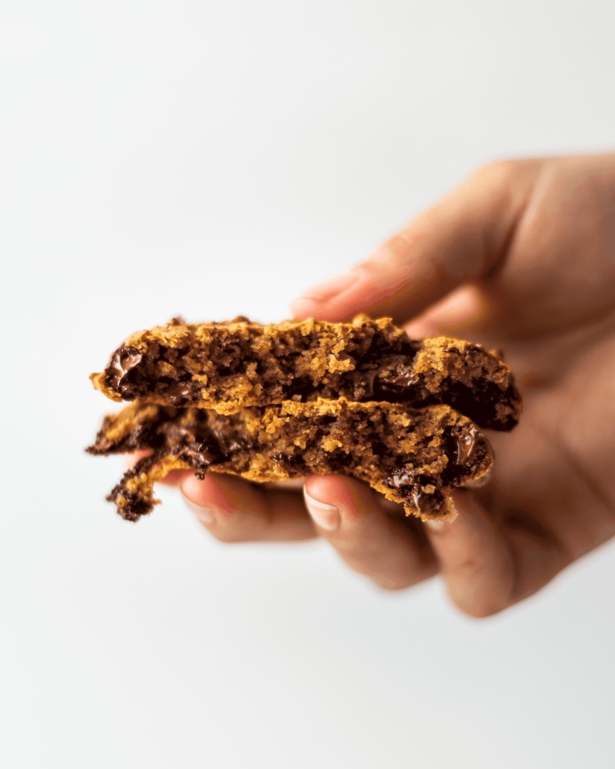 A cookie broken in half, and each half stacked on top of each other, being held to show the melted chocolate chunks inside.