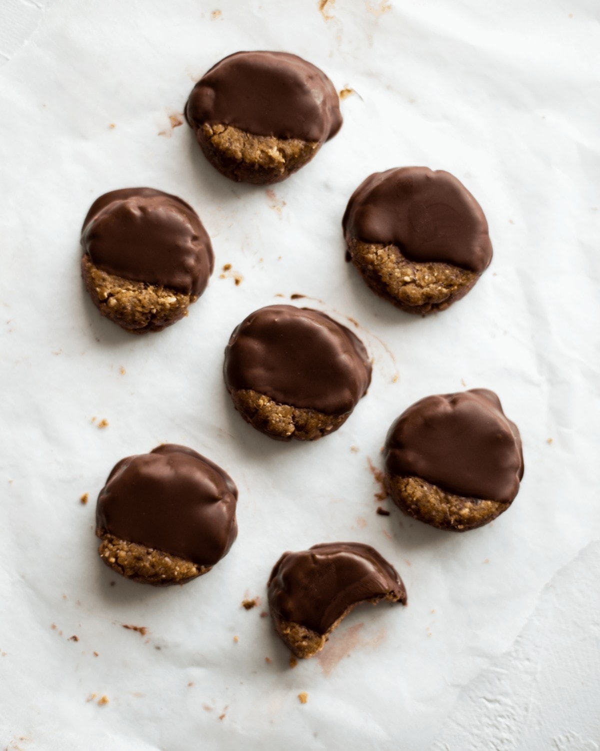 Overhead view of seven chocolate dipped peanut butter cookies, one of which is half eaten by a toddler.