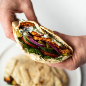 A full Greek tofu pitta, with salad and tzatziki, being held in both hands.