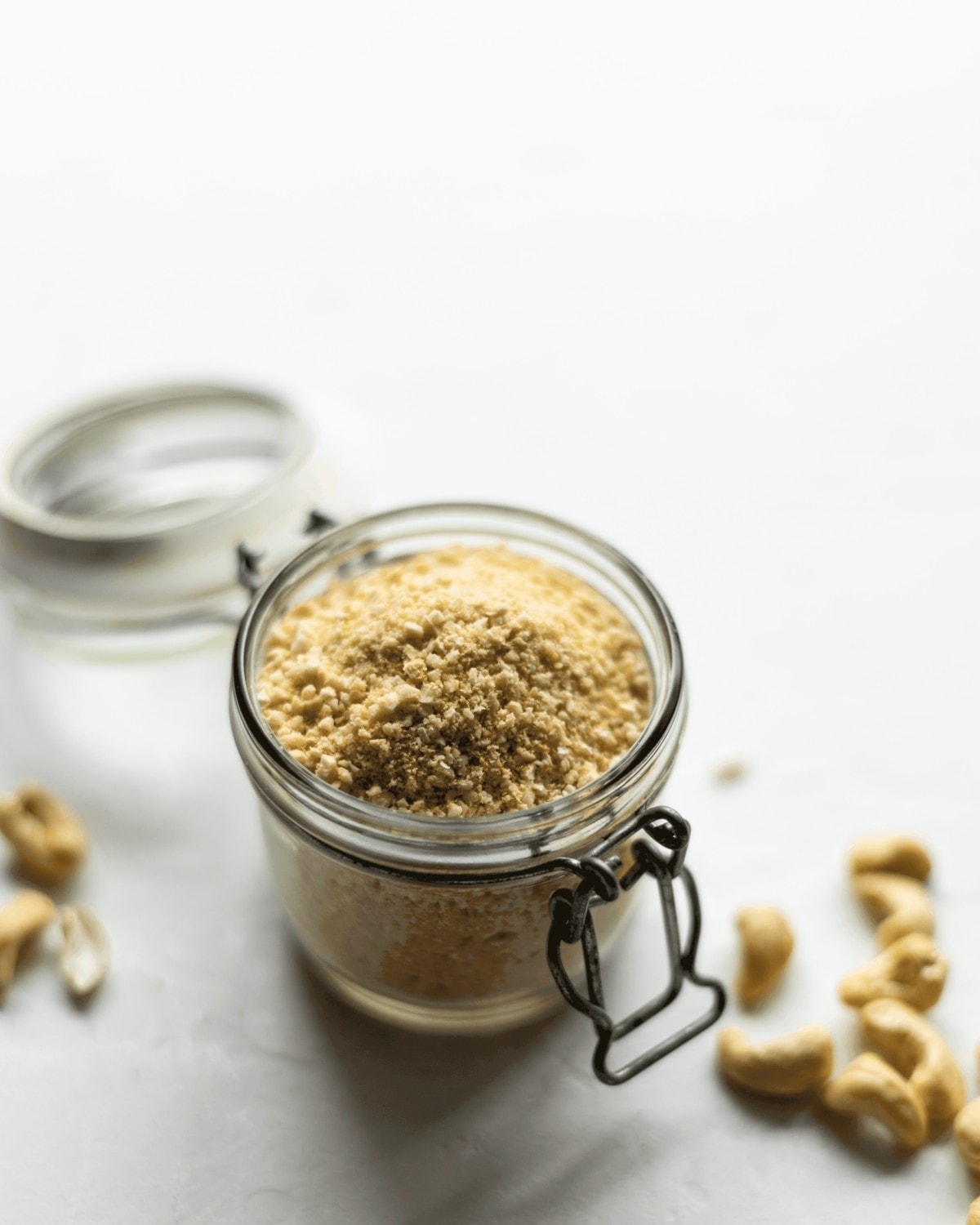 A jar of the vegan parmesan sat on a table with some cashews scattered around.