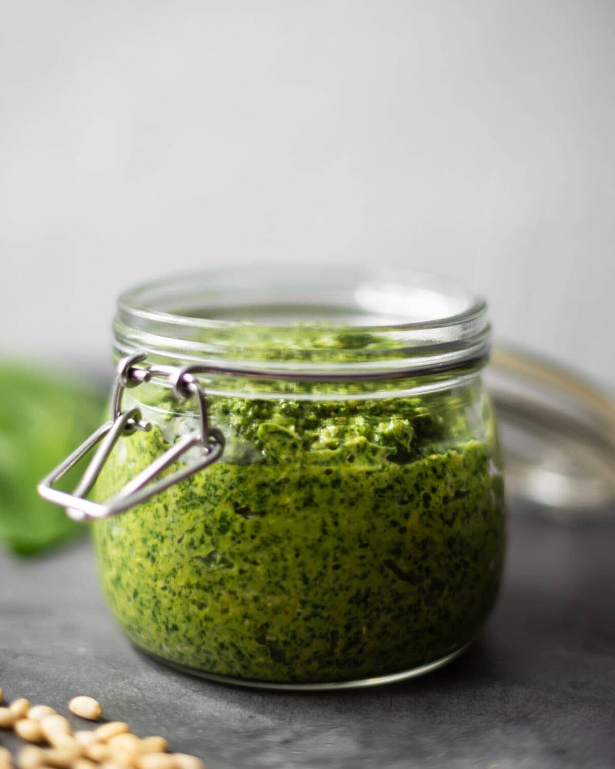 A jar full of the wild garlic pesto, surrounded by wild garlic leaves and pine nuts.