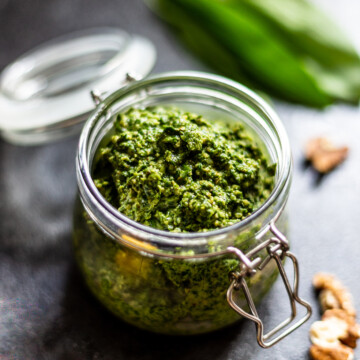 A swing lid jar filled with pesto, surrounded by walnuts and wild garlic leaves.