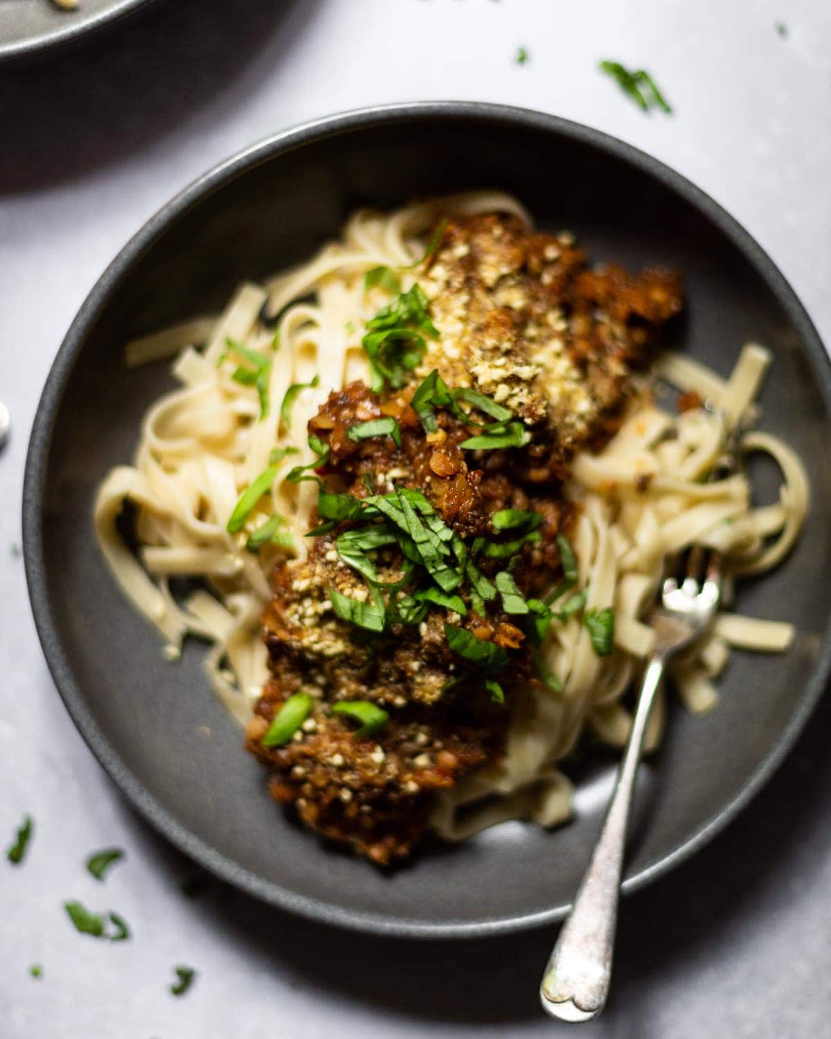 Overhead image of a bowl of fettuccine pasta with vegan lentil bolognese on top, topped with fresh chopped basil and vegan parmesan.