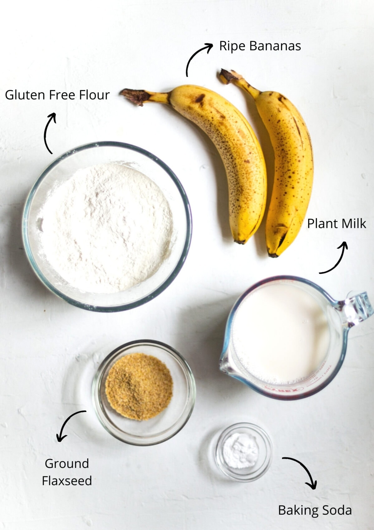 Overhead view of the banana pancake ingredients on a white background, and labelled.