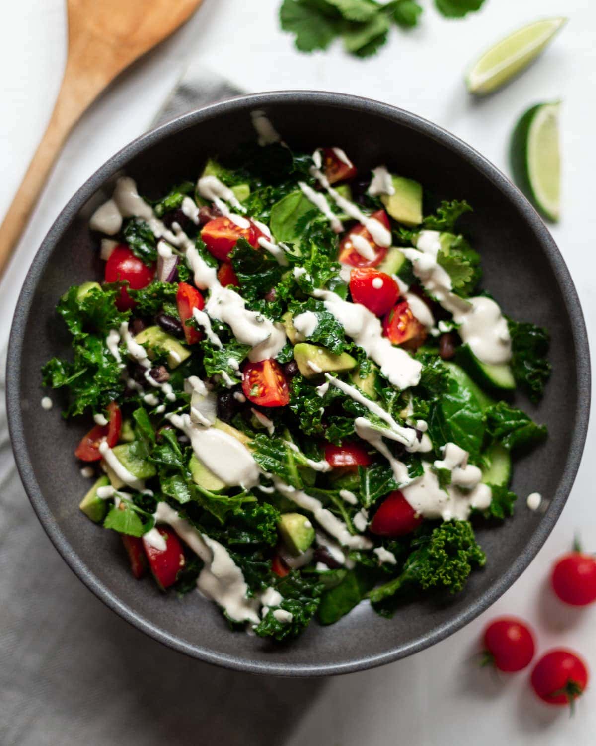 An overhead image of the Mexican kale salad drizzled with garlic cashew cream in a dark grey bowl.