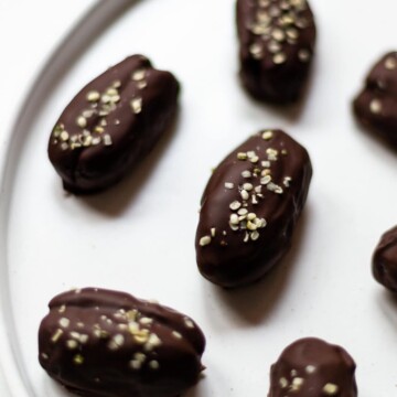 A picture of a white plate with chocolate covered peanut butter dates, sprinkled with hemp seeds.