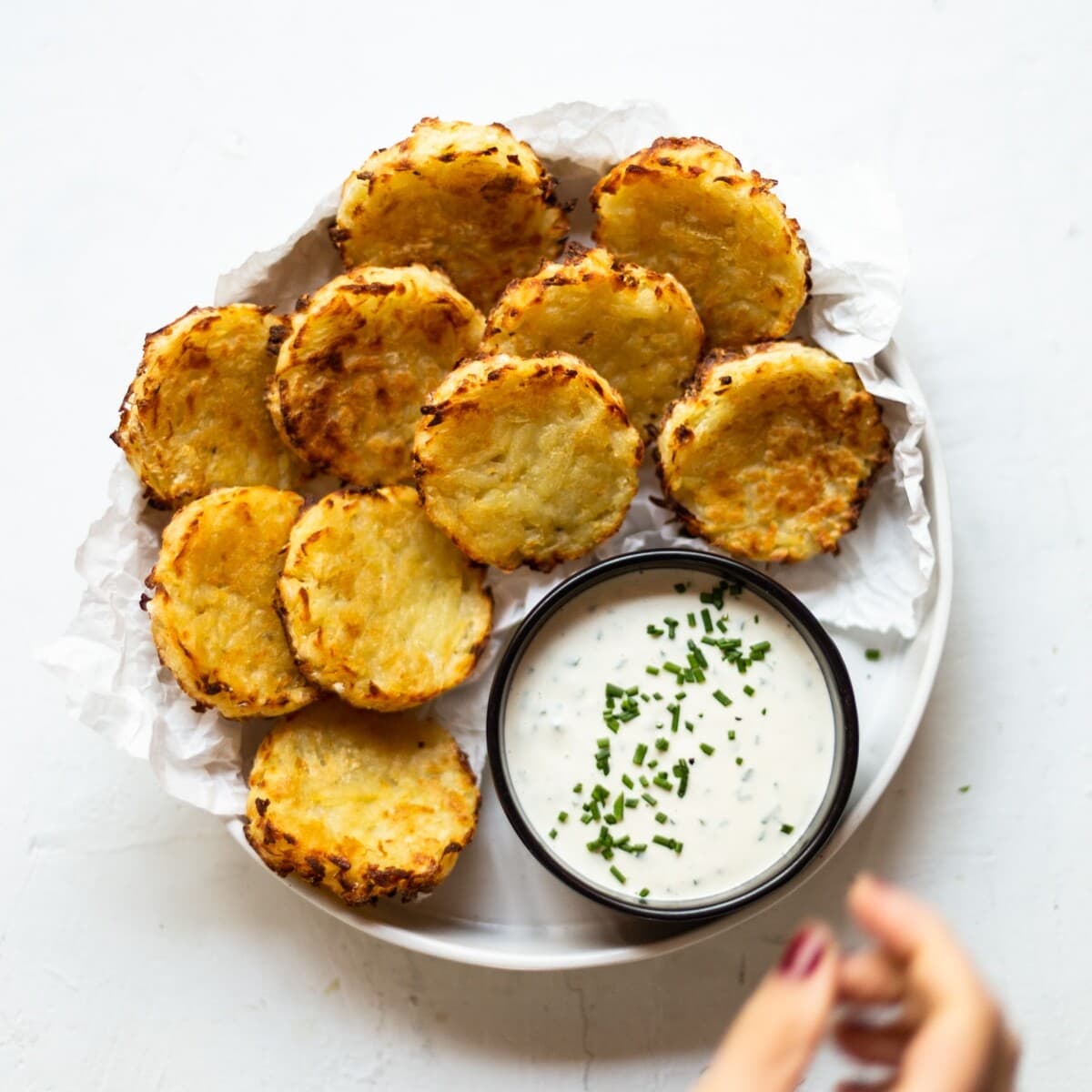 A white ceramic bowl filled with 10 golden, oven baked hash browns, with a separate black bowl of our creamy chive dip.