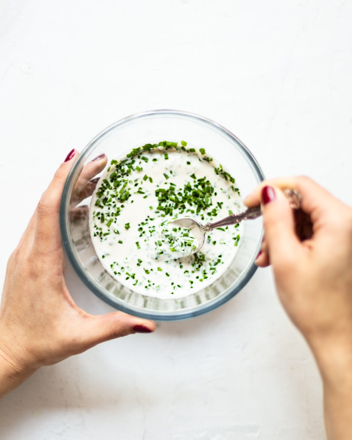 A glass bowl, on a white background, filled with the chive dip being stirred to mix in the freshly chopped chives.
