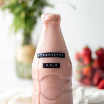 A milk bottle filled with strawberry almond milk, with a little overflowing down the front.